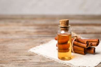 Photo of Bottle with cinnamon essential oil and sticks on wooden table