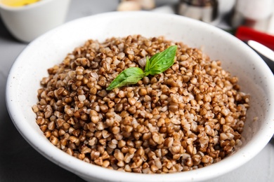 Bowl of buckwheat porridge with basil on table, closeup