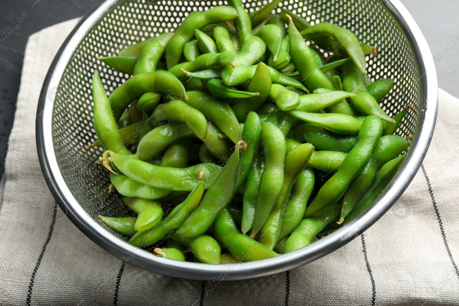 Photo of Sieve with green edamame beans in pods on table