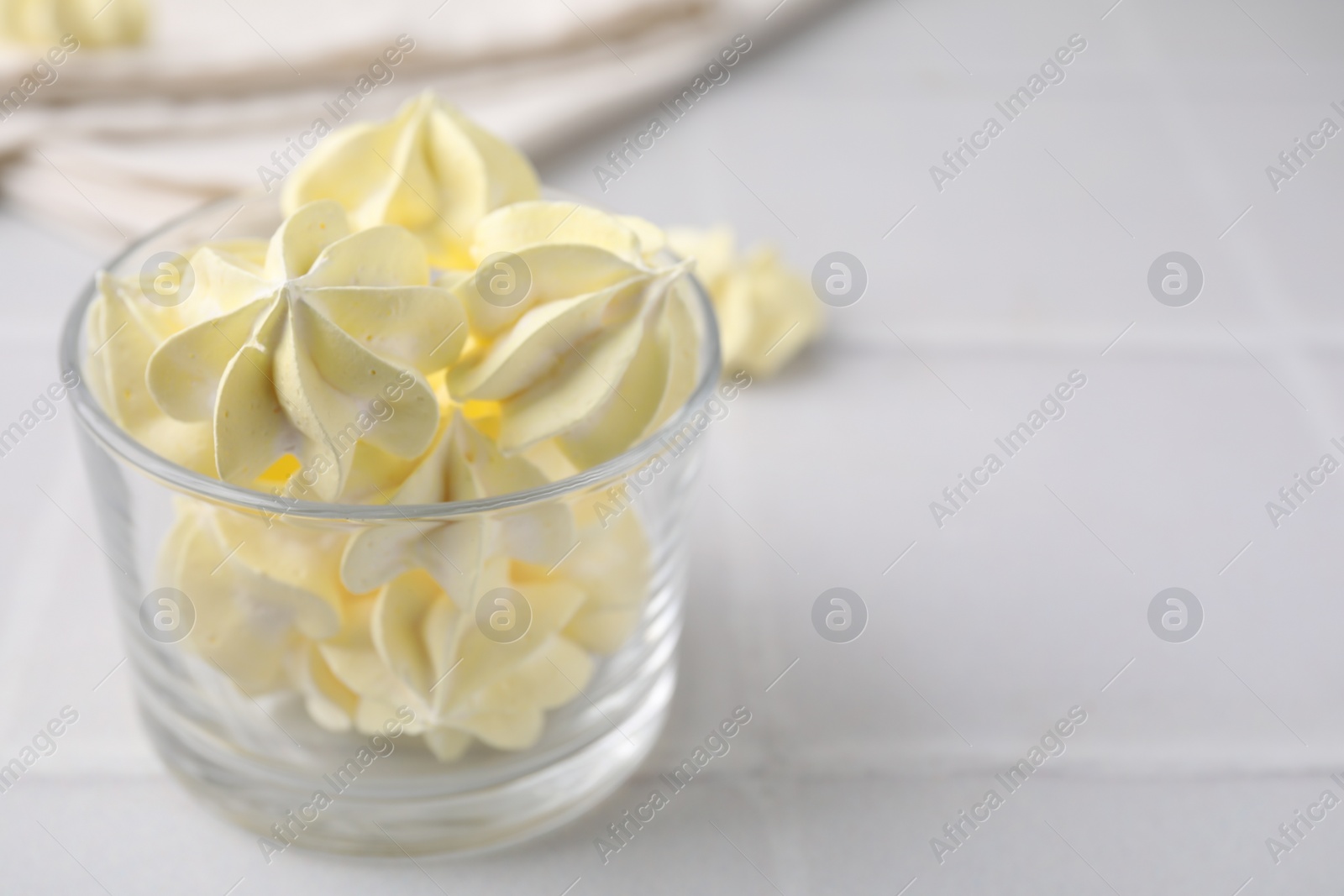 Photo of Tasty meringue cookies in glass on white tiled table. Space for text