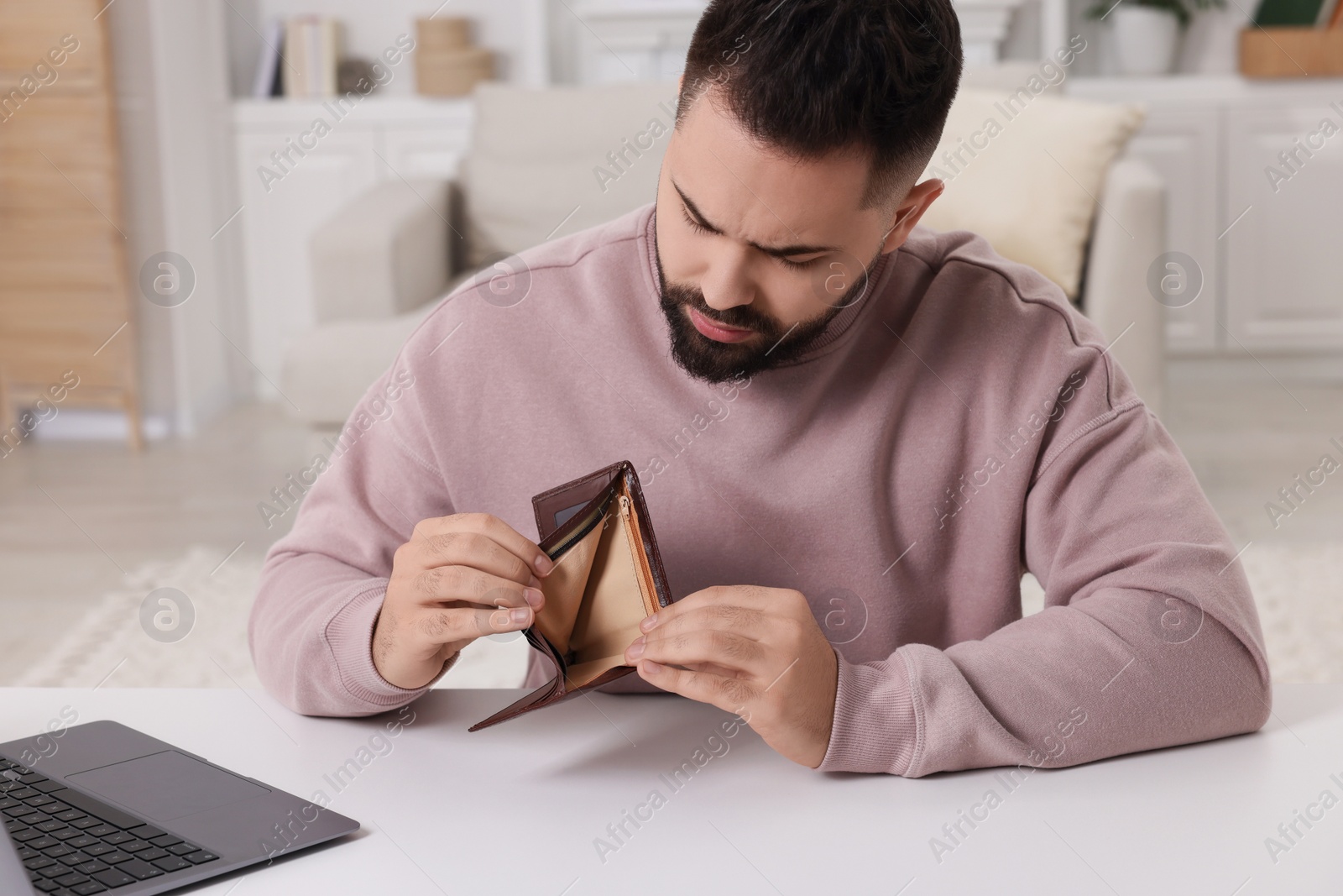 Photo of Upset man with empty wallet at white table indoors