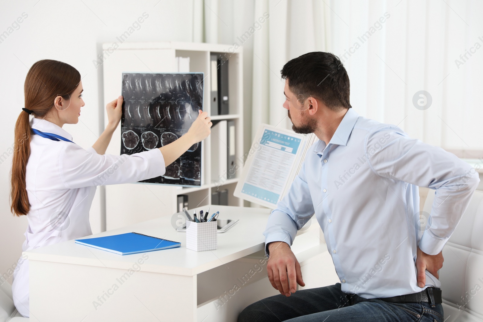 Photo of Orthopedist showing X-ray picture to patient at table in clinic