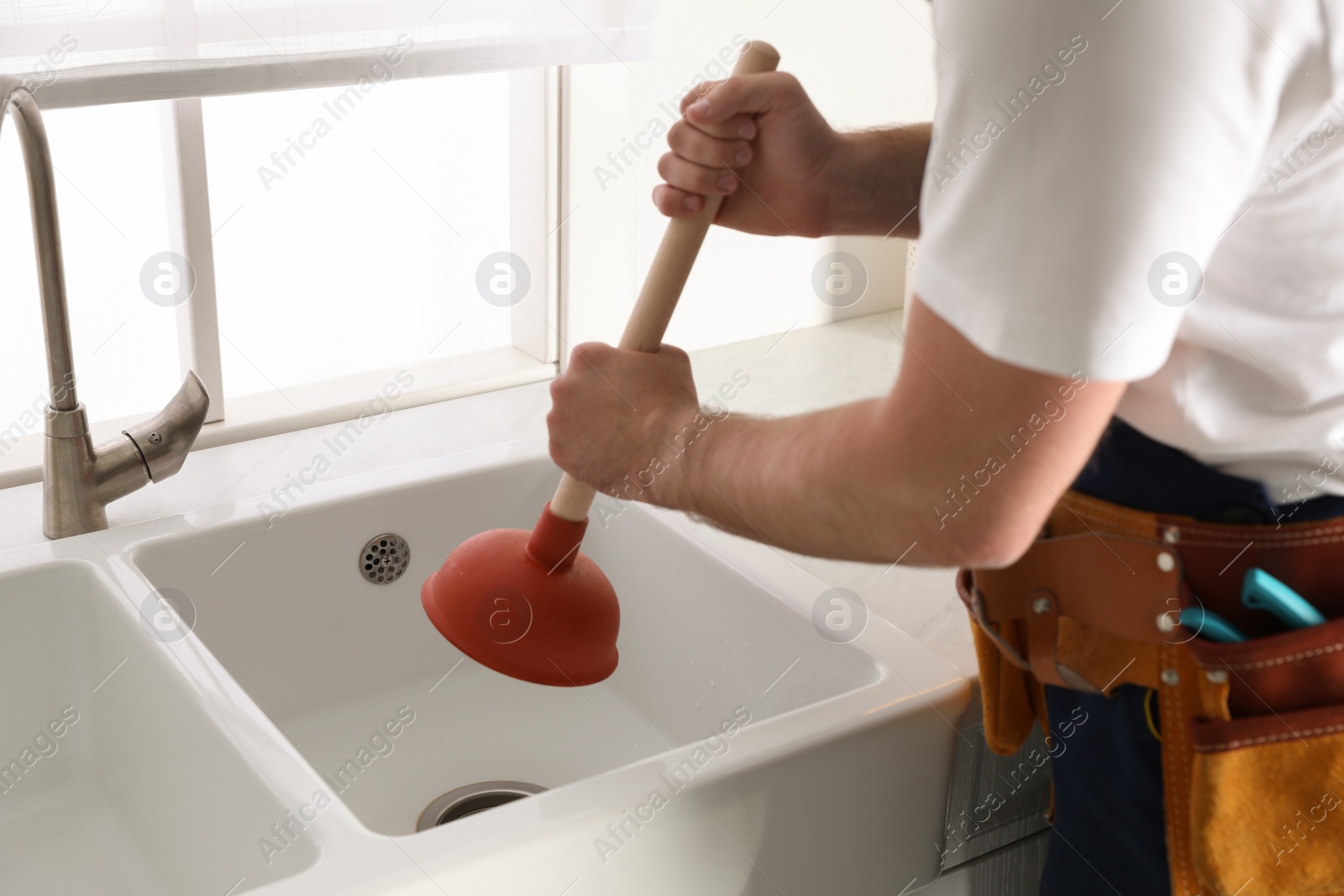 Photo of Plumber using plunger to unclog sink drain in kitchen, closeup