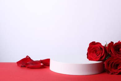 Photo of Stylish presentation for product. Round podium, beautiful roses, petals on red table against white background, space for text