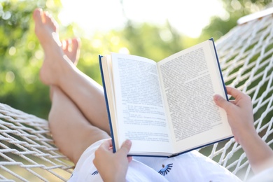 Young woman reading book in comfortable hammock at green garden, closeup