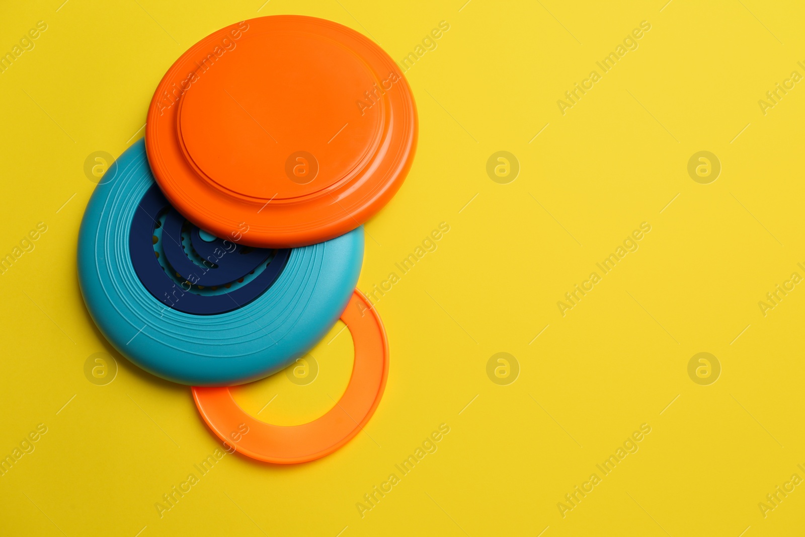 Photo of Plastic frisbee disks and ring on yellow background, flat lay. Space for text