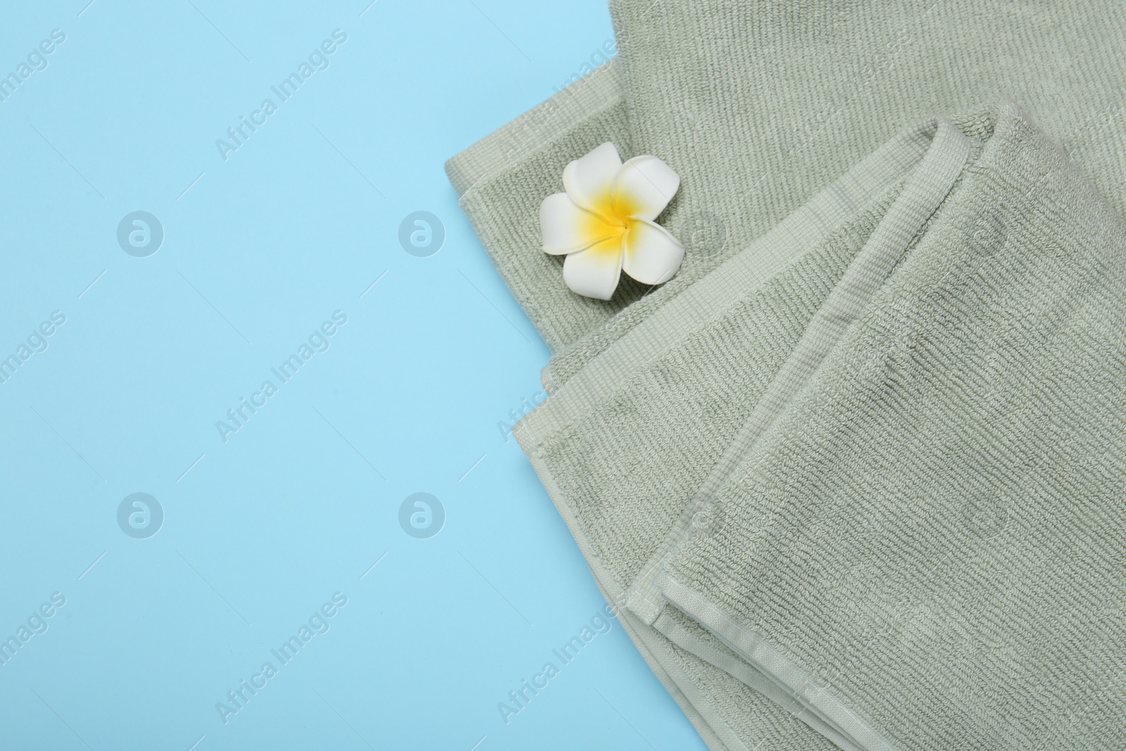 Photo of Terry towels and plumeria flower on light blue background, top view. Space for text