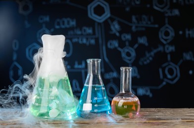 Photo of Laboratory glassware with colorful liquids and steam on wooden table against black background, space for text. Chemical reaction