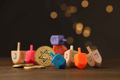 Photo of Dreidels with Jewish letters and coins on wooden table against blurred festive lights. Traditional Hanukkah game