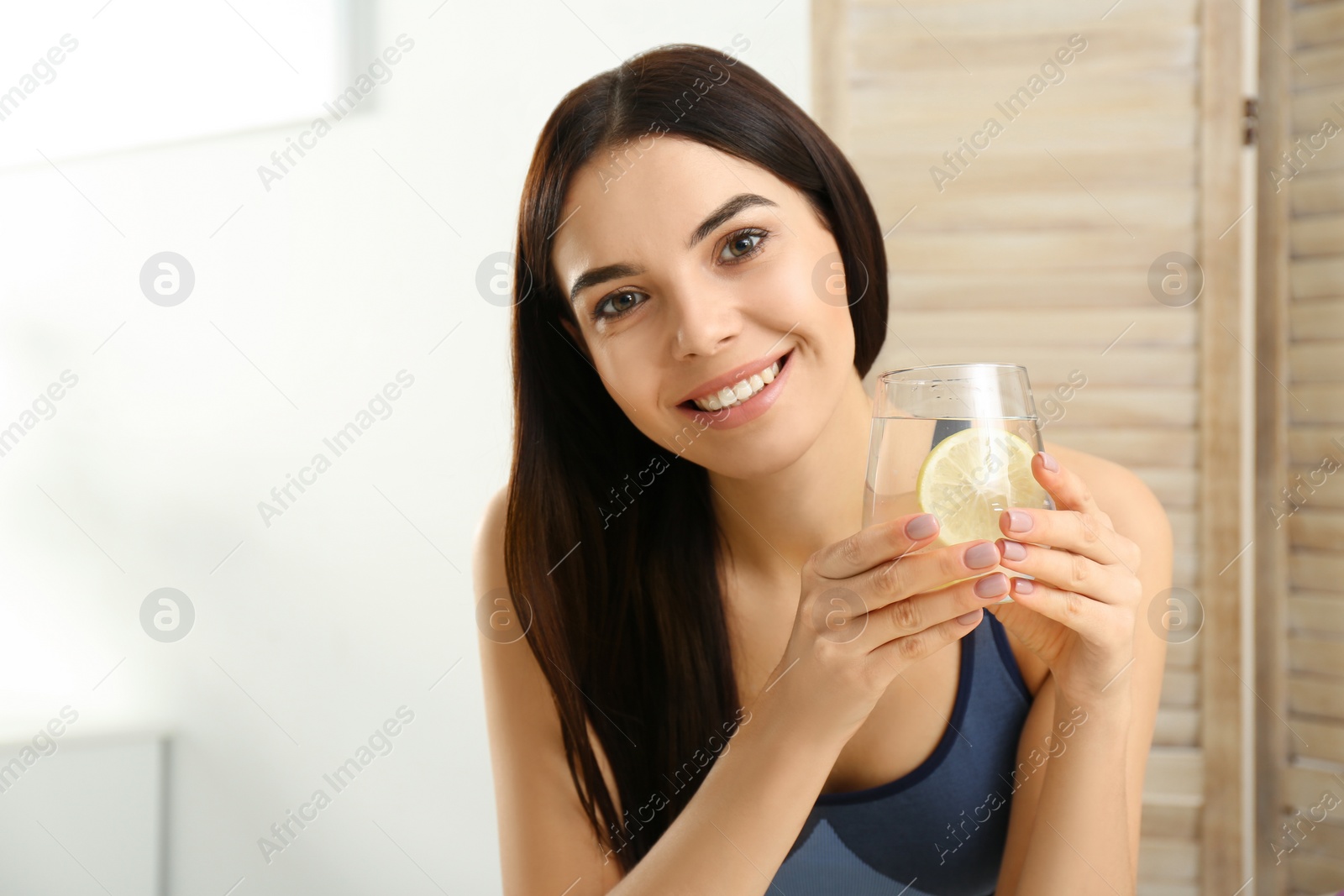 Photo of Beautiful sportive woman with tasty lemon water indoors