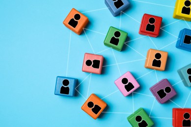 Image of Teamwork. Wooden cubes with human icons linked together symbolizing cooperation on light blue background, top view