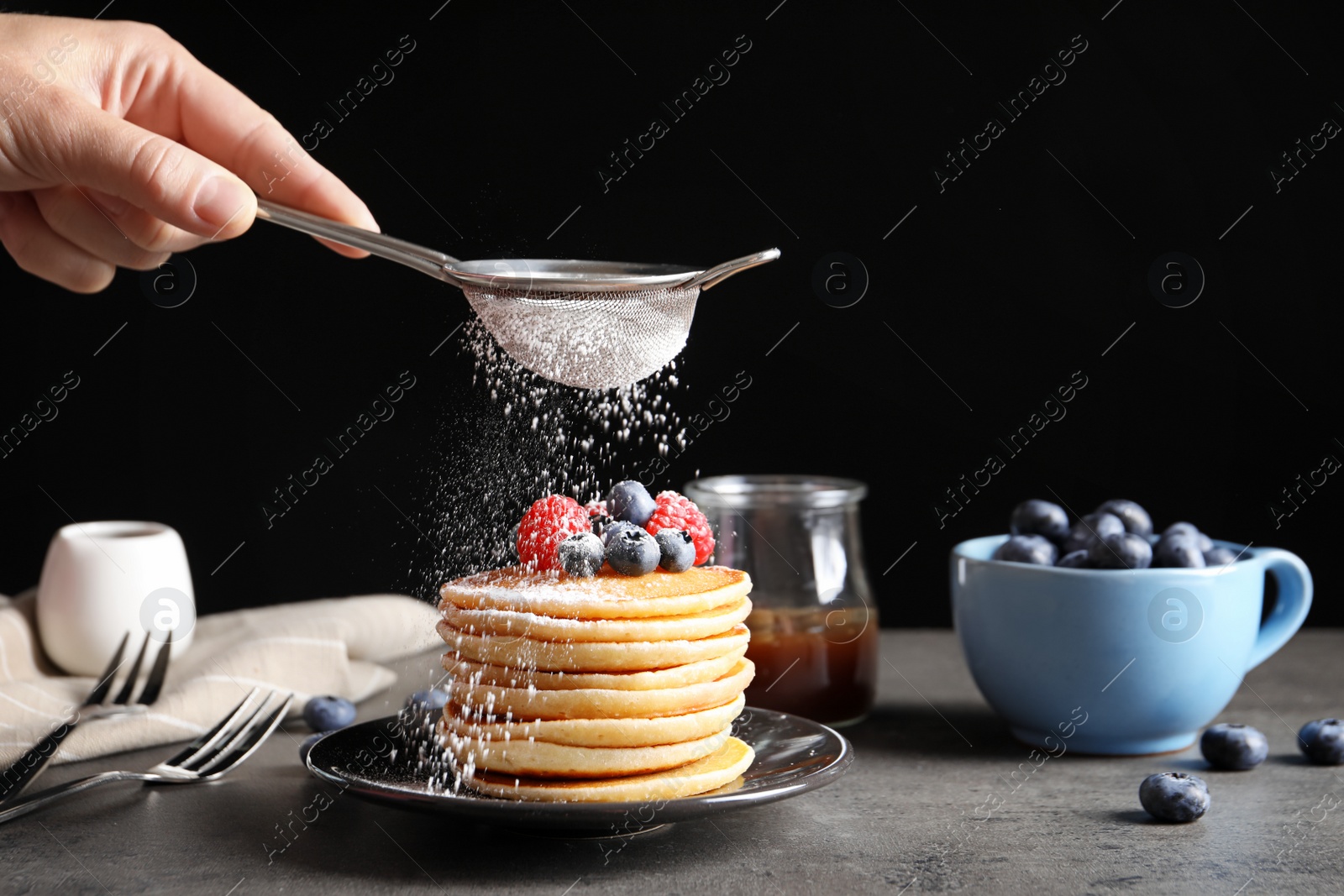 Photo of Woman adding sugar powder to tasty pancakes with berries on plate, closeup