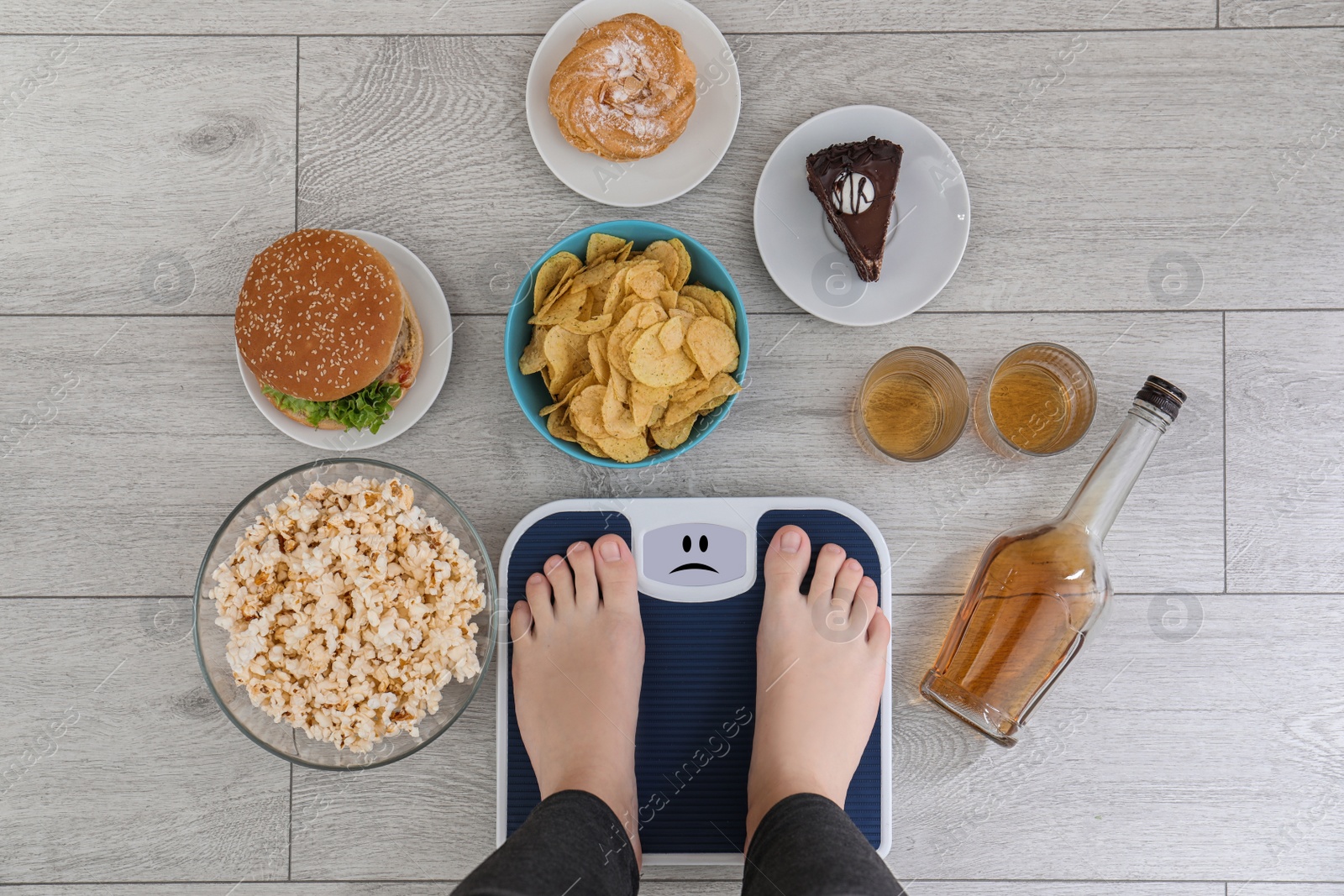 Photo of Woman standing on scales surrounded by different food and alcohol after party indoors, top view