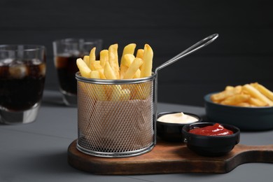 Photo of Tasty French fries, soda, ketchup and mayonnaise on grey wooden table