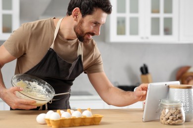 Man making dough while watching online cooking course via tablet in kitchen