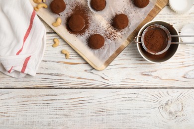 Photo of Delicious chocolate truffles with cocoa powder and nuts on white wooden table, flat lay. Space for text