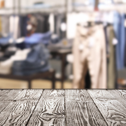 Empty wooden table and blurred view of store with modern clothes