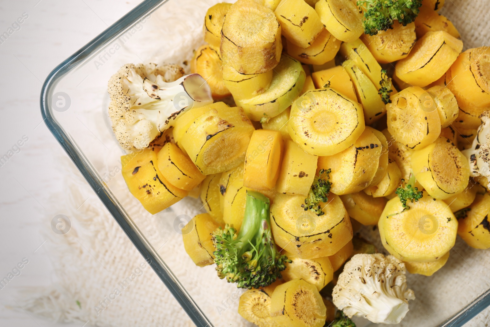 Photo of Baked yellow carrot with broccoli and cauliflowers in glass dish on table, top view