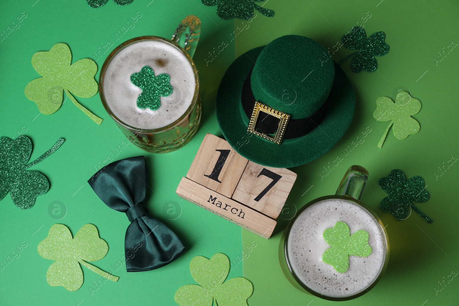 Photo of St. Patrick's day party on March 17. Green beer, leprechaun hat, bowtie, wooden block calendar and decorative clover leaves on green background, flat lay
