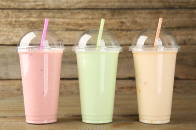 Plastic cups with different tasty smoothies on wooden table