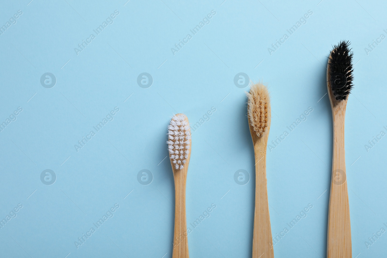 Photo of Bamboo toothbrushes on light blue background, flat lay. Space for text