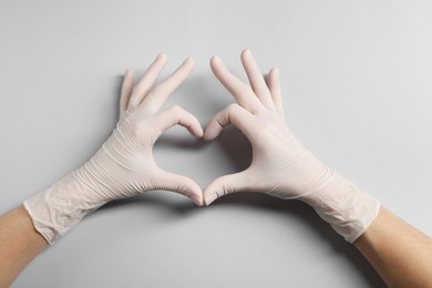 Photo of Doctor wearing white medical gloves making heart gesture on grey background, top view