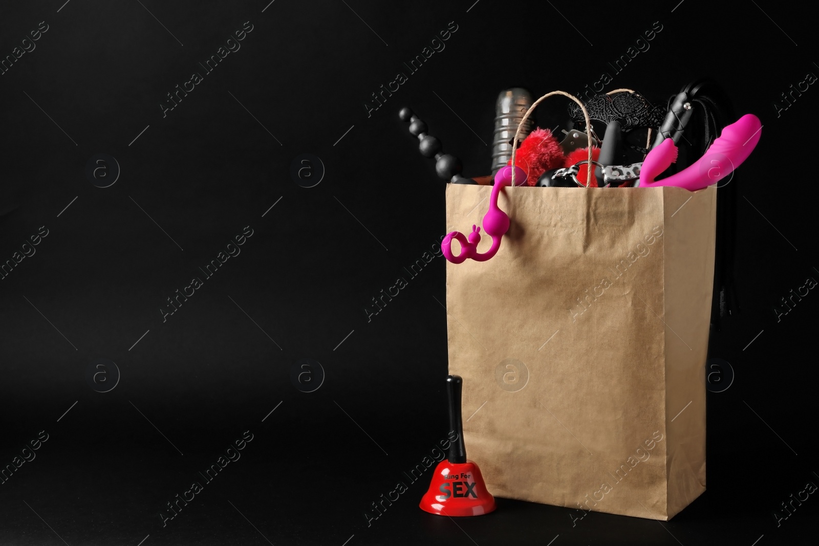 Photo of Paper shopping bag with different sex toys on black background. Space for text