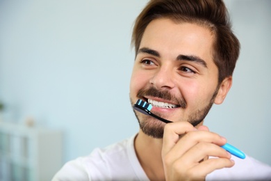 Portrait of young man with toothbrush on blurred background. Space for text