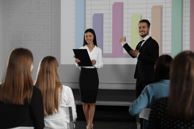 Business trainers giving lecture in conference room with projection screen