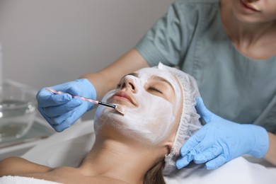 Cosmetologist applying mask on client's face in spa salon