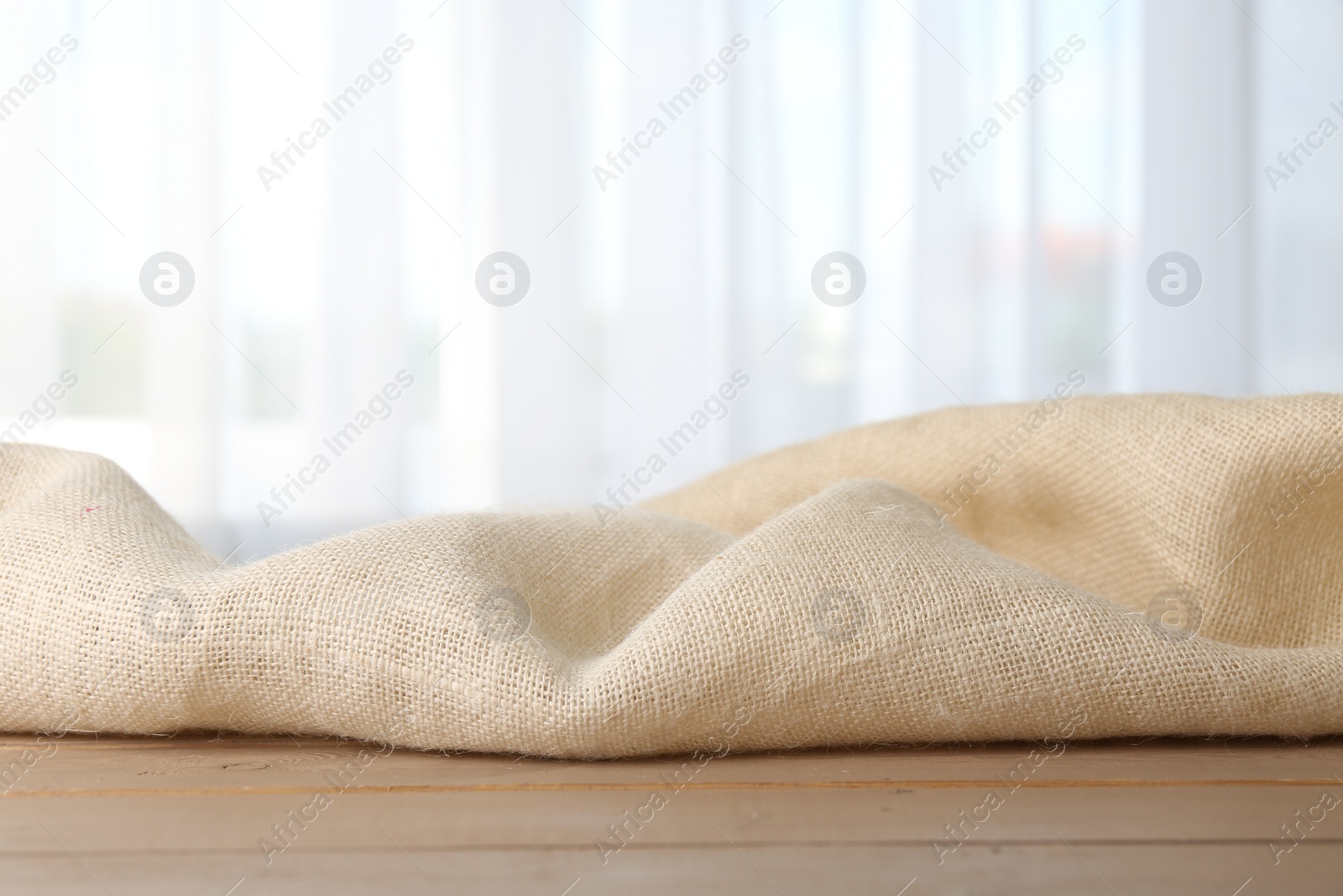 Photo of Beige burlap fabric on wooden table, closeup. Space for text