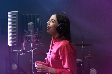 Young singer with microphone recording song in studio