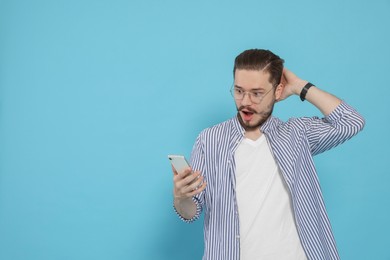 Emotional man with smartphone against light blue background. Space for text