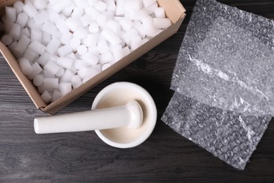 Mortar with pestle, bubble wrap and cardboard box on dark wooden table, flat lay