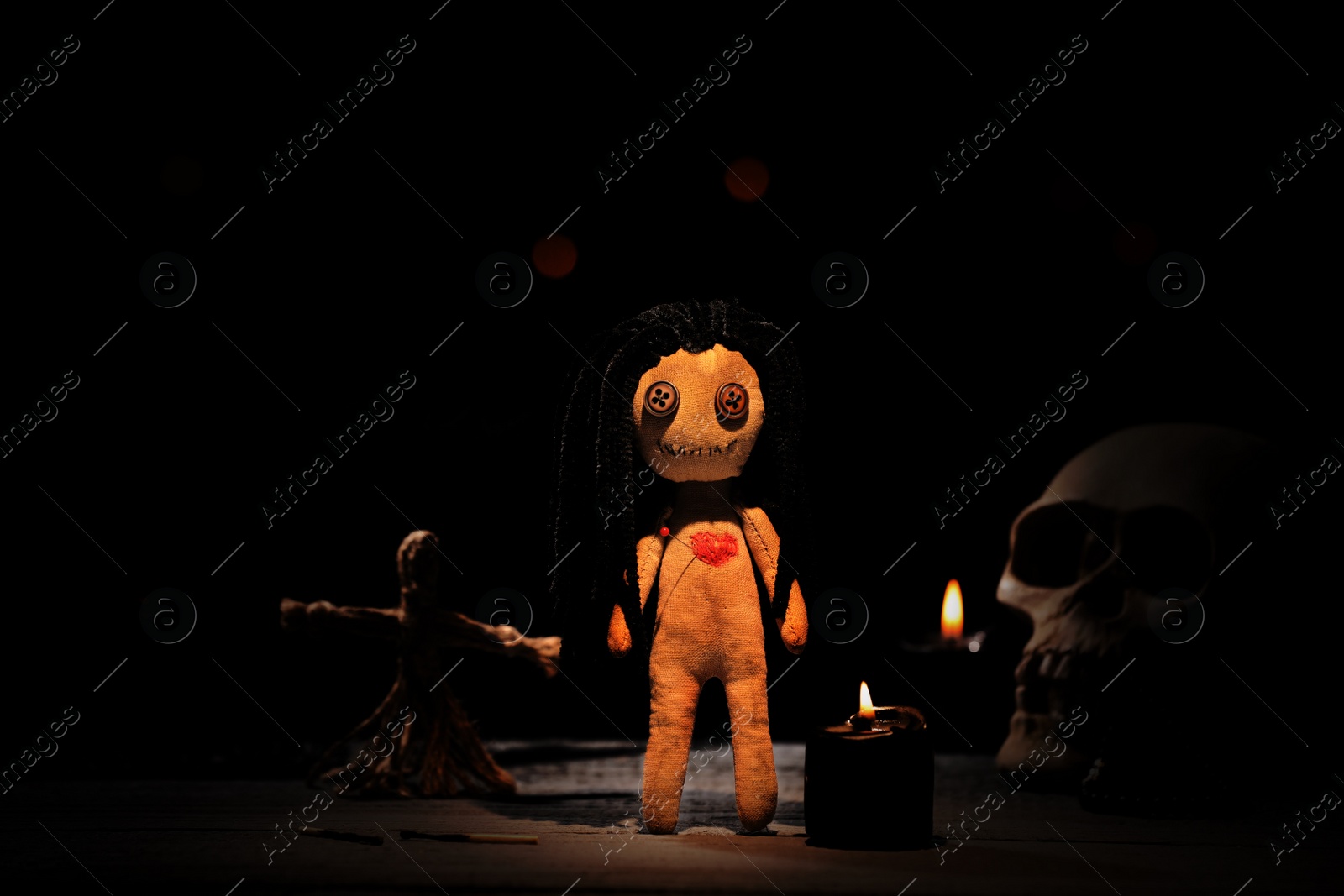 Image of Female voodoo doll with pin in heart and ceremonial items on table in darkness