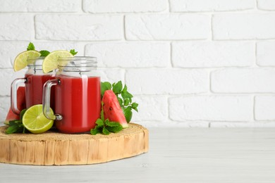 Photo of Tasty summer watermelon drink, limes and mint on white wooden table, space for text