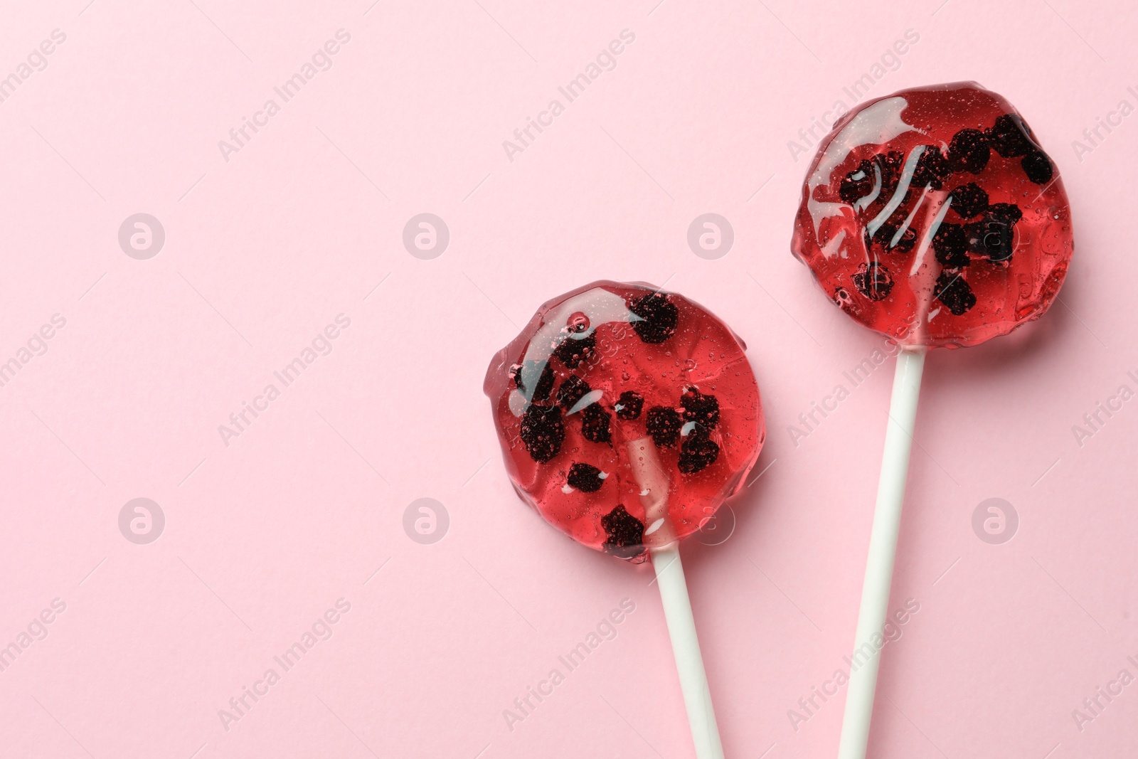 Photo of Sweet colorful lollipops with berries on pink background, flat lay. Space for text