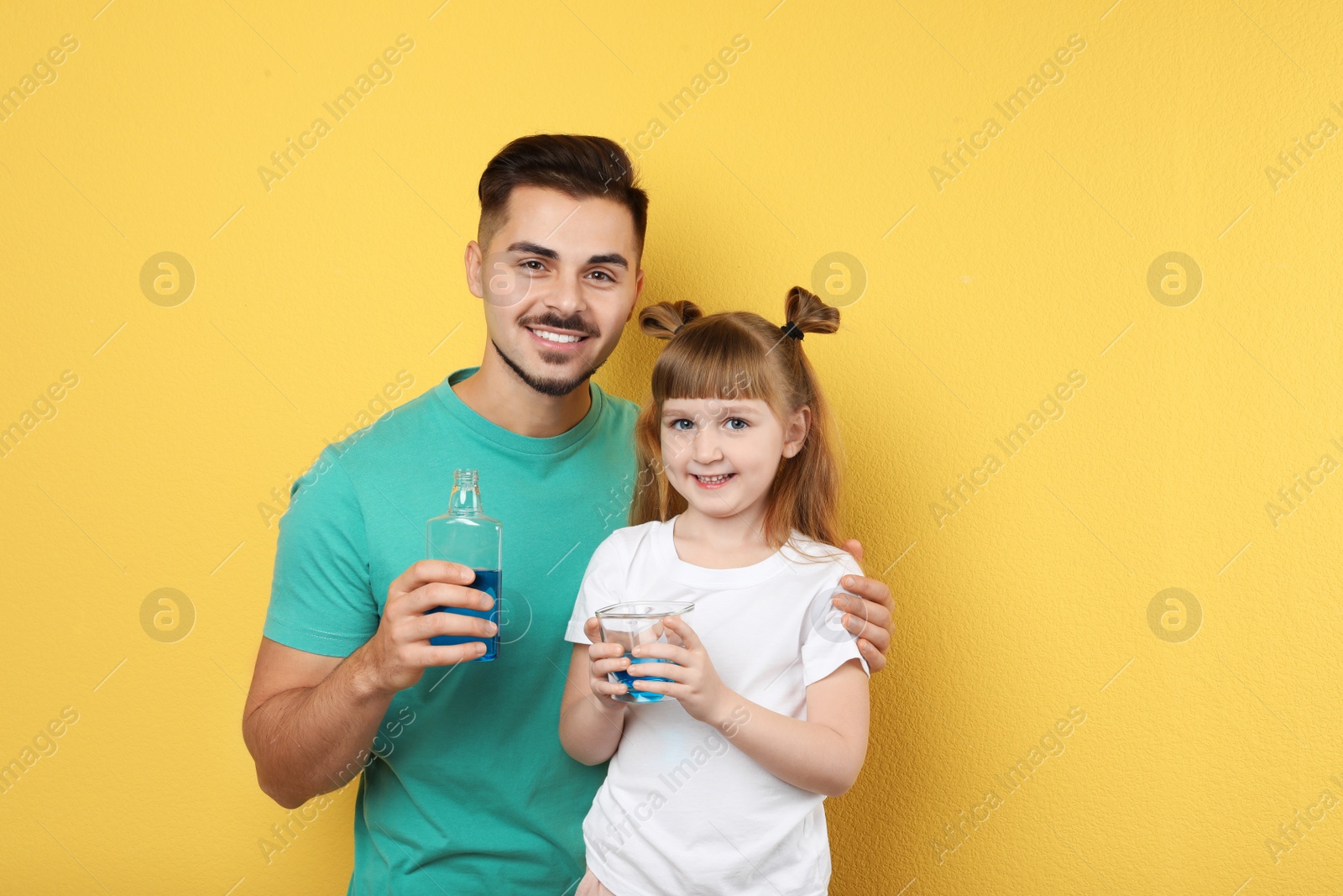 Photo of Little girl and her father with mouthwash on color background, space for text. Teeth and oral care