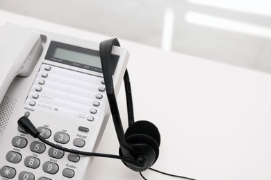 Photo of Headset and desk phone on table, space for text. Technical support concept