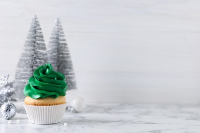 Delicious cupcake with green cream and Christmas decor on white marble table. Space for text