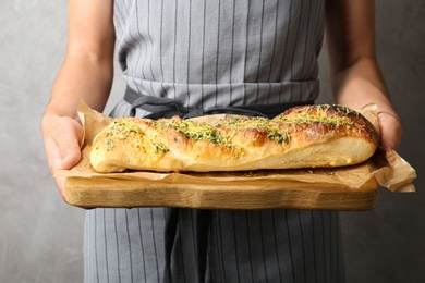 Photo of Woman holding tasty homemade garlic bread with cheese and herbs against grey background