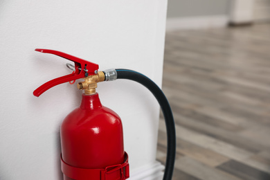 Photo of Fire extinguisher near white wall indoors, closeup. Space for text