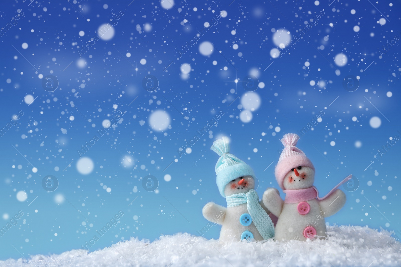 Image of Cute snowmen in snow against blue background, bokeh effect. Space for text 