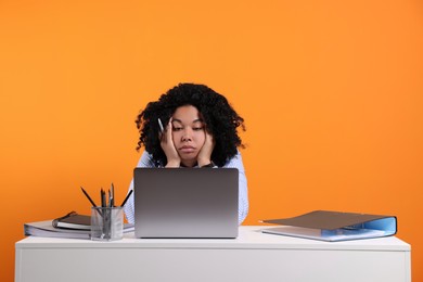 Stressful deadline. Tired woman looking at laptop at white table on orange background