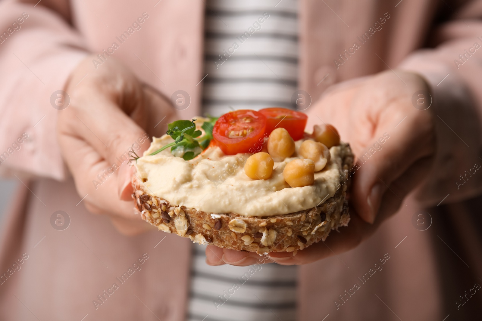 Photo of Woman holding delicious sandwich with hummus , tomato slices and chickpeas , closeup