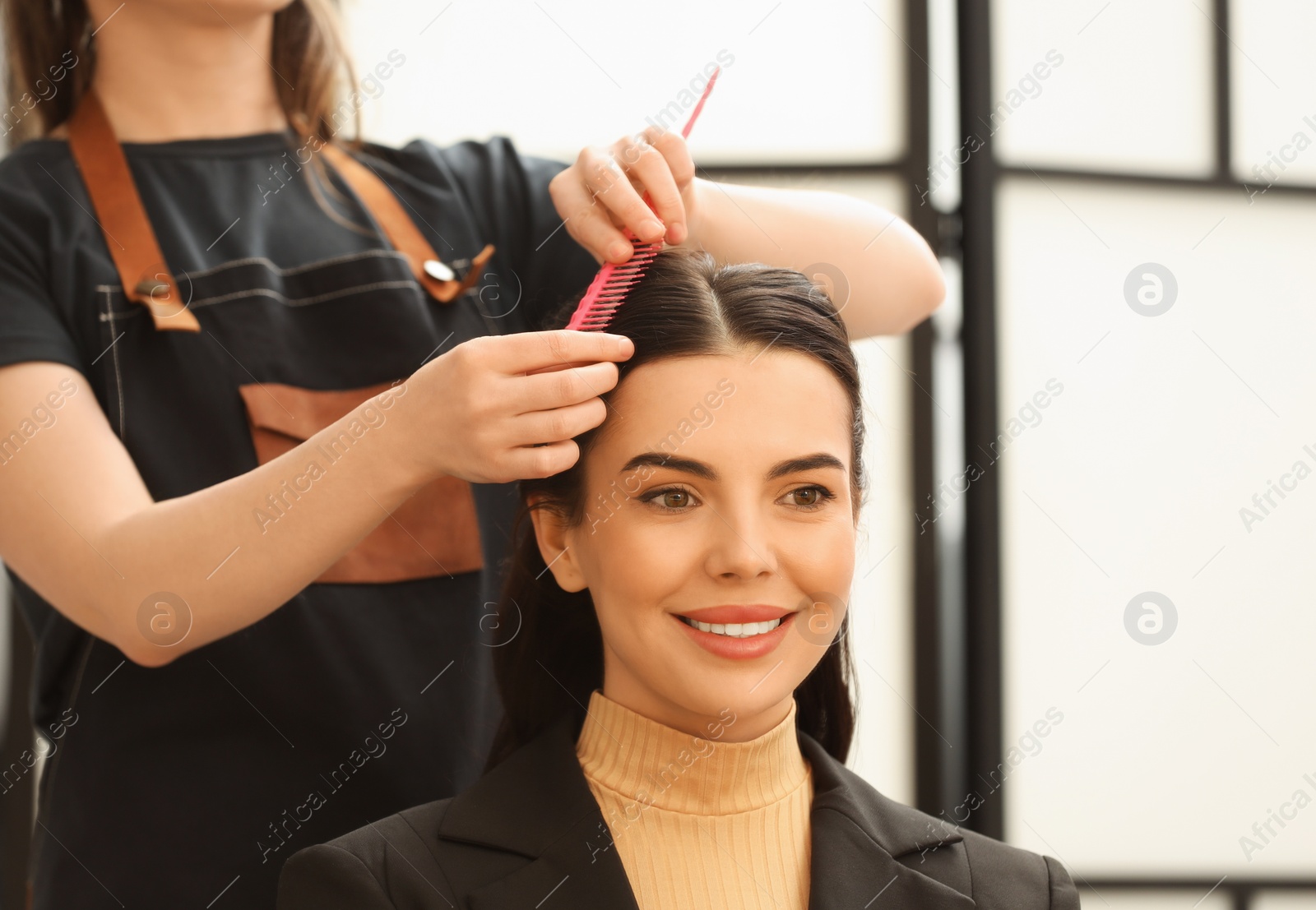 Photo of Hair styling. Professional hairdresser combing woman's hair indoors, closeup