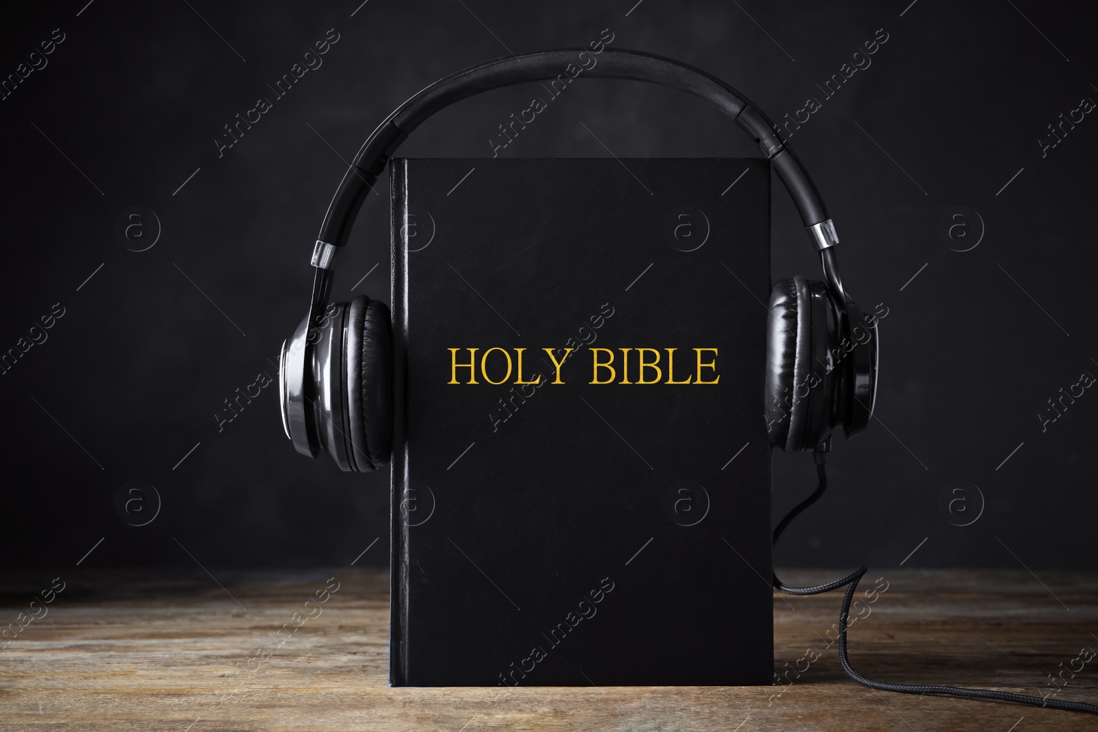 Photo of Bible with headphones on wooden table. Religious audiobook