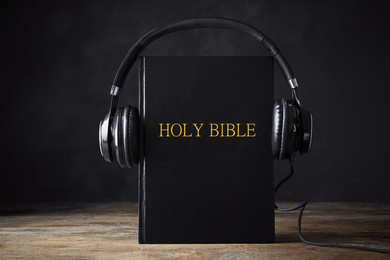 Photo of Bible with headphones on wooden table. Religious audiobook
