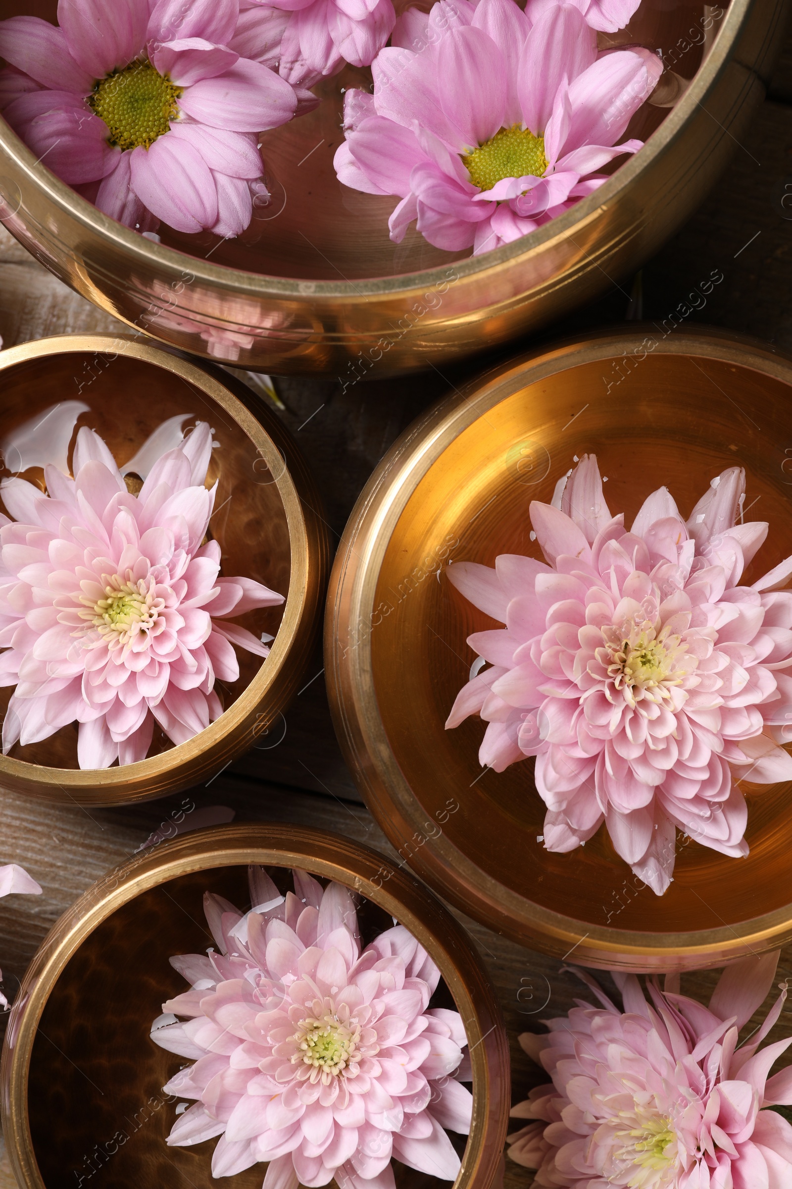 Photo of Tibetan singing bowls with water and beautiful flowers on wooden table, flat lay