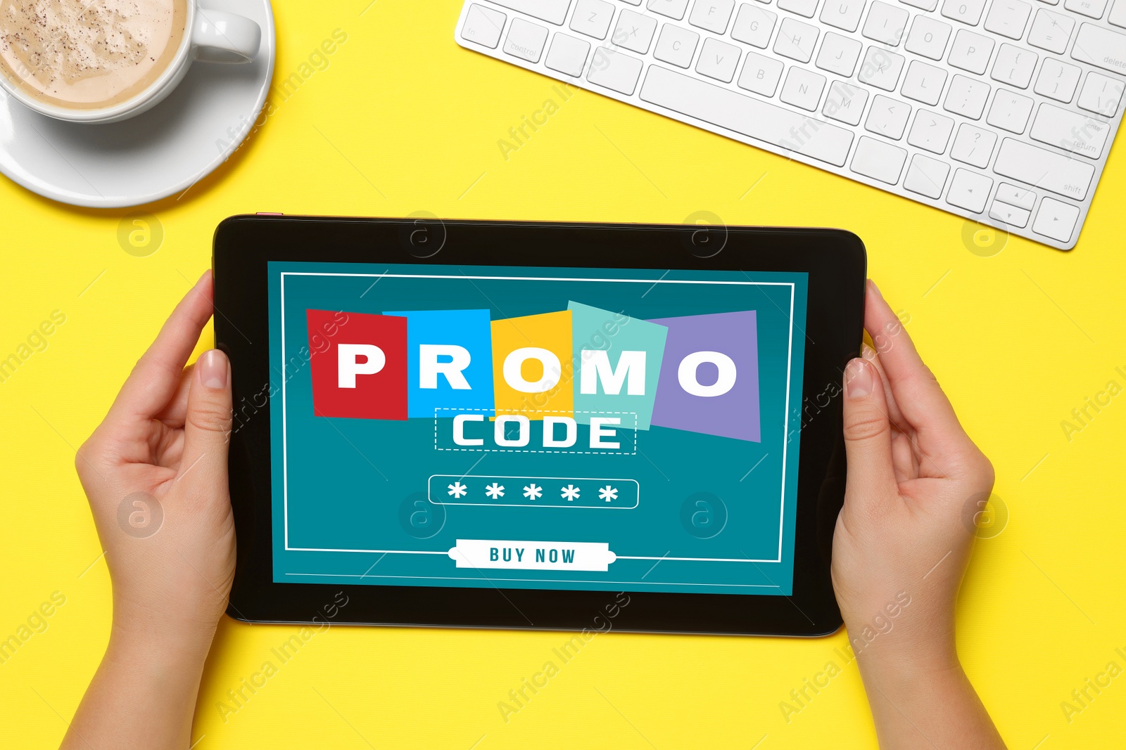 Photo of Woman holding tablet with promo code at yellow table, top view